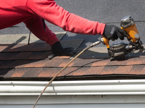 Roofer with nail gun attaches shingles after performing chimney flashing and repair in Mattoon IL