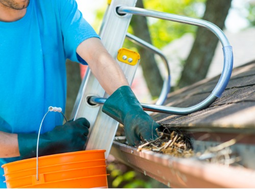 A worker is seen removing debris from gutters. Popejoy Roofing offers Gutter Cleaning in Mahomet IL.