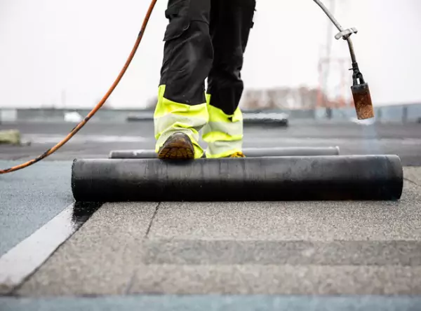 A roofing contractor rolling out new flat roofing for a commercial building, with roofing products from Versico Roofing Systems